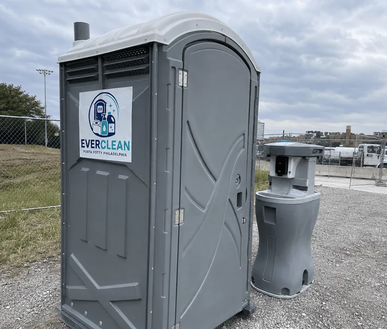 Porta potty and hand sanitizer stand on a fenced job site with the city skyline behind